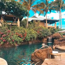 Woman wades in small outdoor swimming pool with rocks, waterfall and tropical gardens