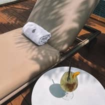 A green cocktail is set on a table next to an upholstered pool lounge chair