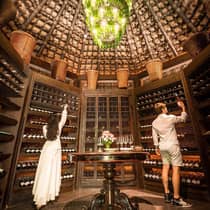 Man and woman select bottles of wine from walls of dome shaped cellar under chandelier