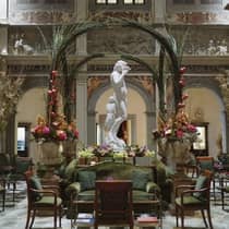 Opulent interior with a white marble statue, green seating, floral arrangements and decorative arches in a grand hall with detailed wall carvingss.