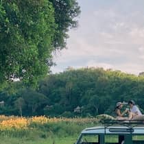 Two guests sit on top of a safari vehicle in a field