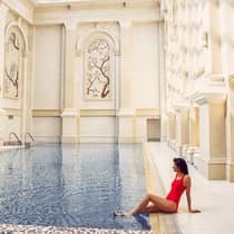 A woman in a red swimsuit lounges at an indoor pool surrounded by ornate architecture