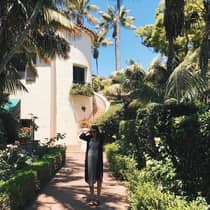 Woman in dress, sunglasses stands on garden path in front of sunny Honeymoon Suite, outdoor staircase
