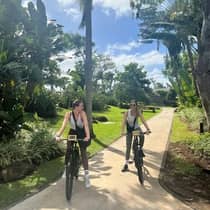 Two guests dressed in athletic attire ride bicycles on a tree-lined path