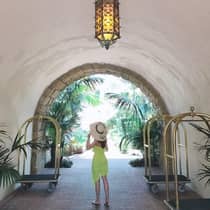 Back of woman with straw sunhat, dress standing under lantern, curved cement archway