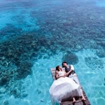 Bride and groom lay on dock over blue lagoon, boat in background