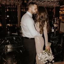A romantic moment captured as a couple dressed in wedding attire lean in for a kiss in the chic ambiance of a bar, illuminated by soft lights