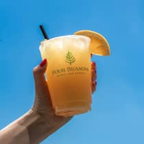 Guest holding orange drink with straw and orange slice on the glass.