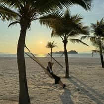 A guest relaxing in a hammock on a beach at sunset