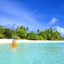 Woman kayaks in clear blue water with view of the island
