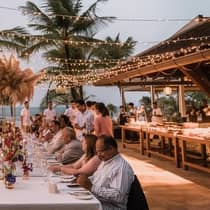 Guests enjoy dinner at a tropical outdoor reception under string lights