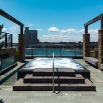A square hot tub on a terrace with stone floors and columns overlooking a water view with a city skyline behind