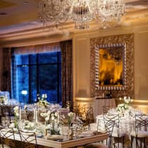 Ballroom with table and chairs, white roses and chandelier lighting with window view. 