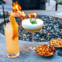 Two cocktails, bowls with chips and nuts on edge of patio fireplace