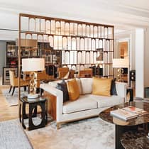 Elegant living area featuring a cosy sofa with gold accent pillows, stylish lamps, a chic coffee table and a modern room divider with arch motifs