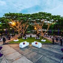 Guests and servers stand in a lit courtyard filled with tables, chairs and plush white sofas 