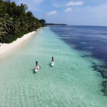 Two women on paddle boards float through crystal clear water next to the beach