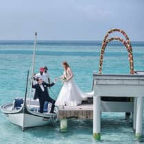 Groom helps bride into canoe at dock of overwater wedding ceremony on lagoon
