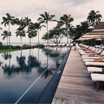 Tall palm trees reflected on outdoor swimming pool lined with lounge chairs