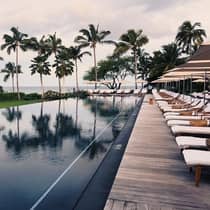 Tall palm trees reflected on outdoor swimming pool lined with lounge chairs