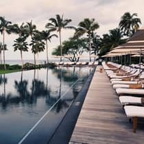 Tall palm trees reflected on outdoor swimming pool lined with lounge chairs