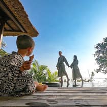 Family wearing robes, young child sits cross legged on patio as parents hold hands in background