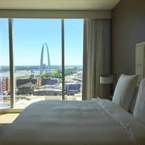 Luxury hotel room with a large window view of the St. Louis Gateway Arch, featuring a neatly made bed with white linens and natural light streaming in