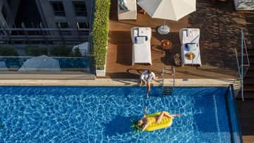 Woman lays on yellow floatie in pool, situated on top of building