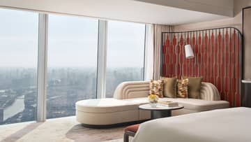 Sleek hotel room featuring a large ivory-coloured chaise next to a wall of windows overlooking city