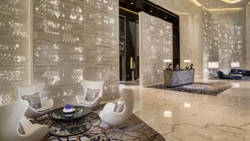 Four white mid-century style armchairs around glass table in lobby with white decorative panels, marble