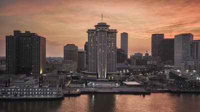 The exterior of a tall building next to a body of water with a city in the background.