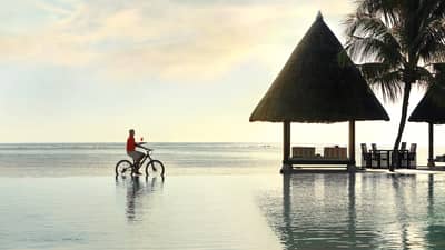 A server riding a bike balances a cocktail on a tray along oceanfront lounge