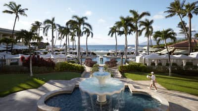 Historic 1990s photo of staff carrying towels past large fountain to outdoor pool, deck at resort