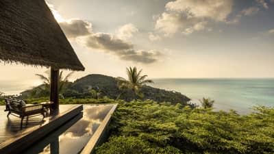 Patio lounge chair, thatched roof and deck overlooking canopy of tropical trees, ocean