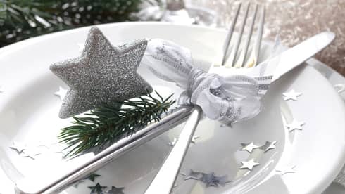 White dinner plate decorated with festive silver star confetti and motif, small fir tree cutting, and silverware tied with bow of white ribbon