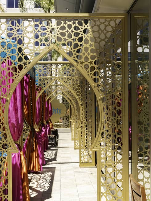 A row of golden Arabesque-style arches create a walkway on an outdoor patio with magenta curtains tied to one side