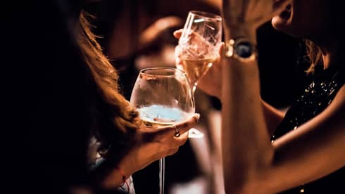 Close-up of women's hands holding wine, cocktail glasses in dark lounge