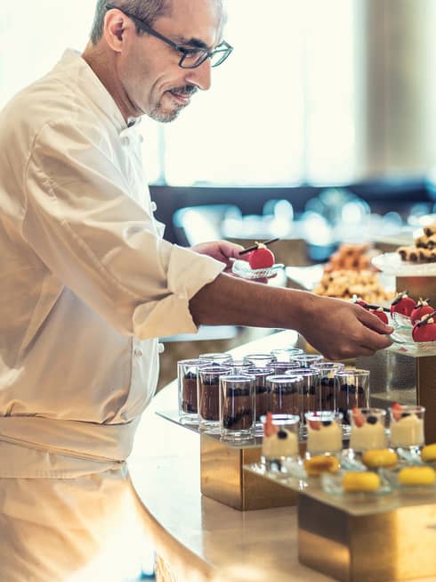 A chef prepares several chocolate pastries inside a patisserie.