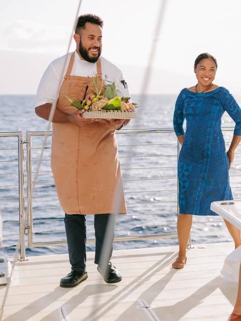 A group of four tourists smile at chef presenting tray of food on a boat
