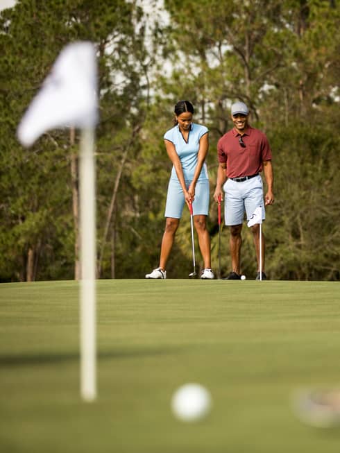 View past golfer to smiling couple preparing to putt on golf course