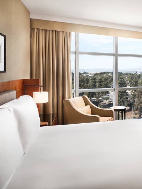 Close-up of hotel room bed, gold armchair under curtain, window
