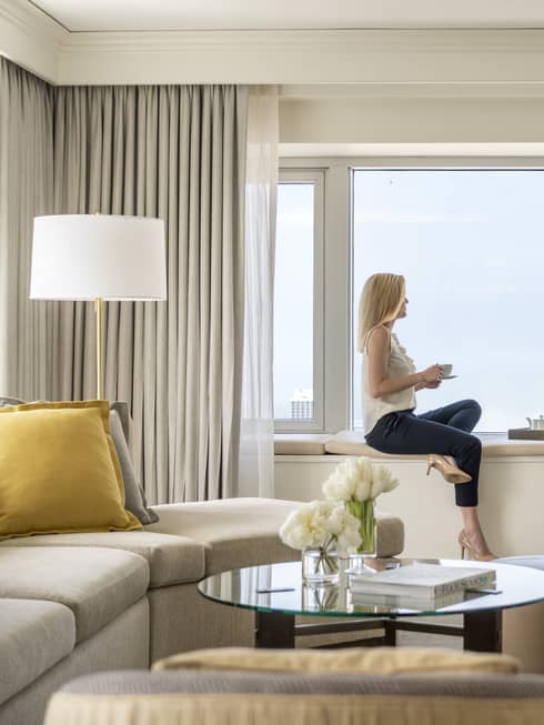 A woman hold a cup of tea and sits on a windowsill in a One Bedroom Suite