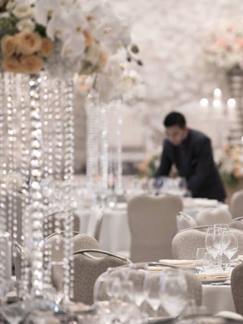 Hotel staff sets elegant ballroom banquet tables with white flowers, crystal ware 