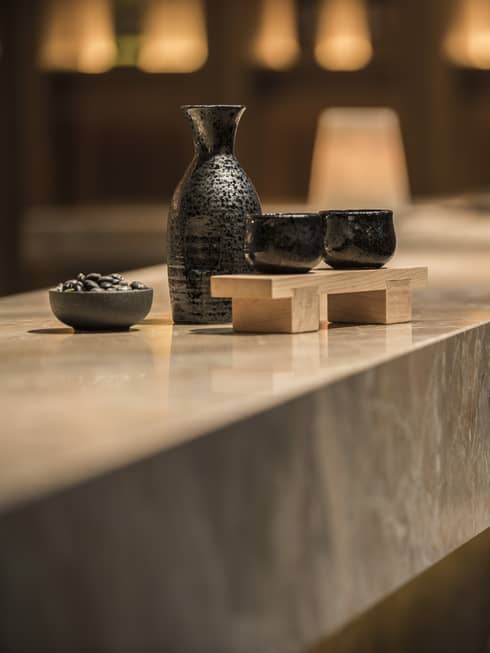Close-up of black sake jug with two cups on wood tray on marble bar