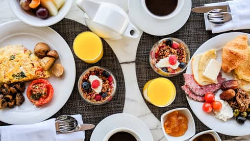 Aerial view of brunch table with omelette, cheeses, meats, croissants, cups of granola and yogurt