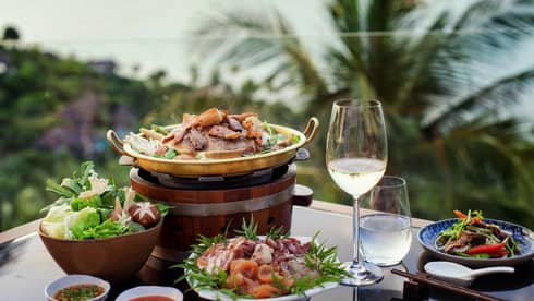 Four plates of food, glass of water and white wine, tropical scenery in background
