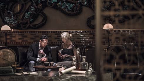 Man, woman drink cocktails on dark leather lounge sofa in Charles H lounge