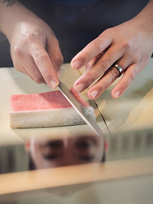 Person cutting a pink piece of food on a counter into slices