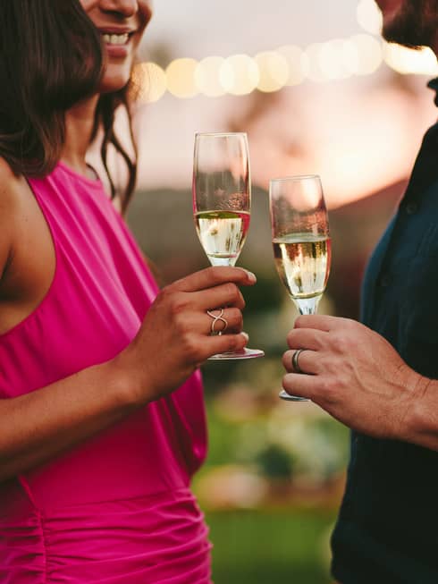 A woman in a fuscia pink dress hold a glass of champagne next to a man with a navy shirt holding his own glass 
