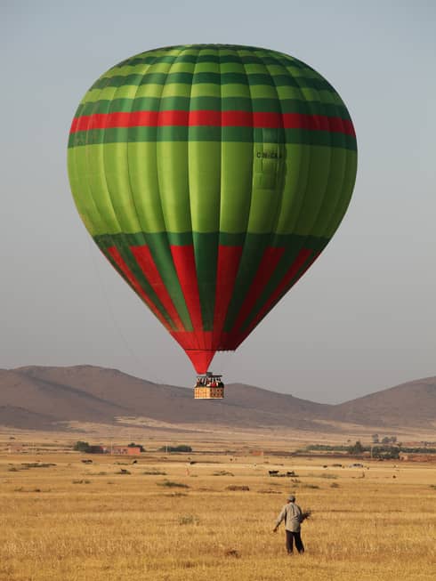 Man stands in field under large green and red hot air balloon 